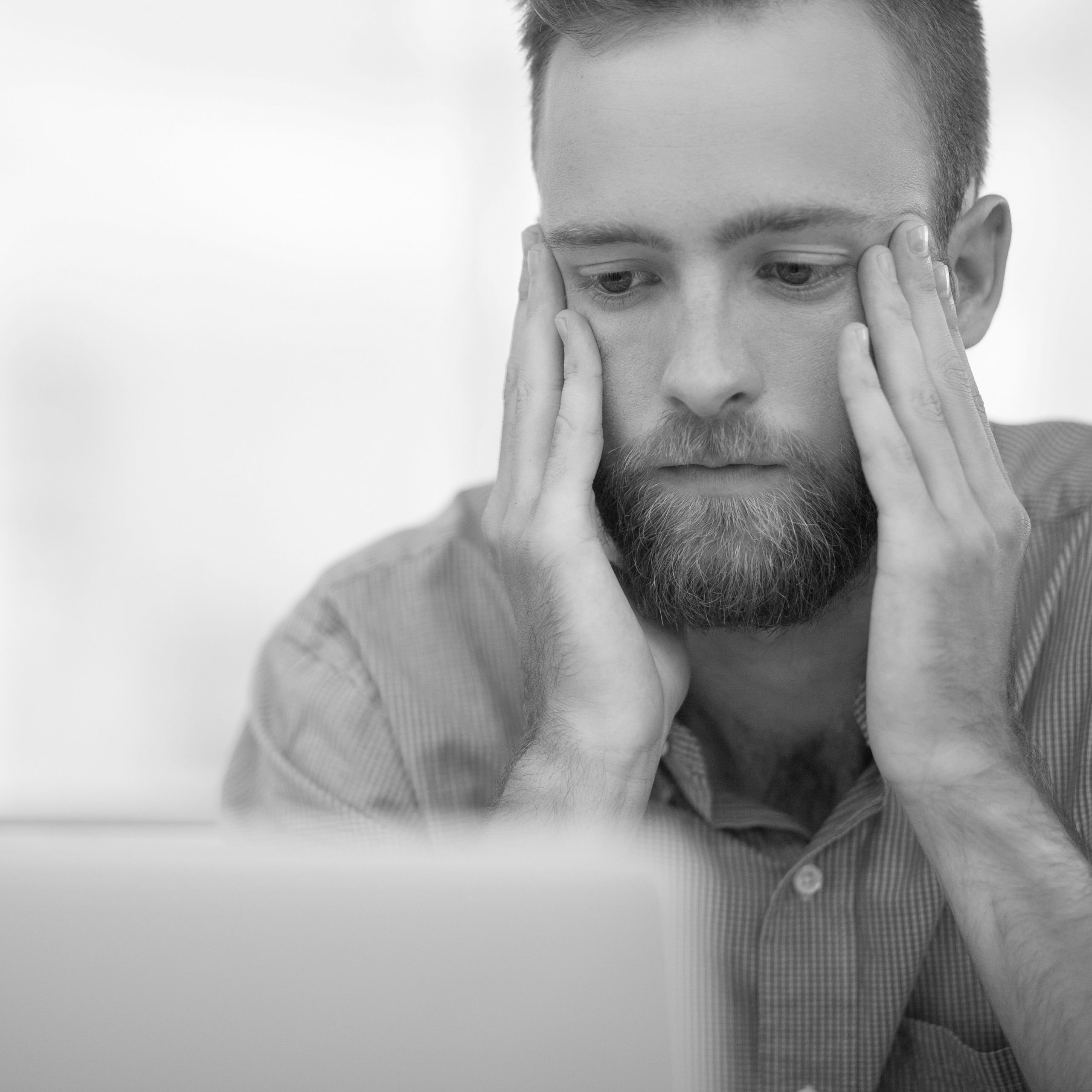 Young bearded Caucasian manager sitting in office in stress and having trouble while working at laptop